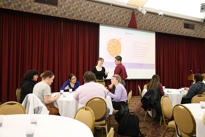 Students, faculty and staff sit at tables tasting Jewish cultural food.