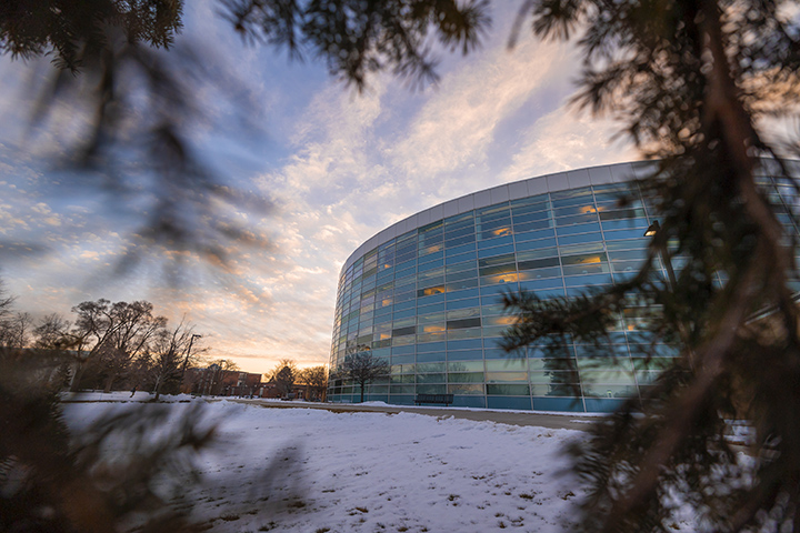 The sun sets behind the Charles V. Park Library as snow rests on the ground in the foreground.