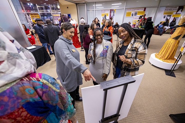 Three people look at a display board while surrounded by various CMU student and alumni-designed clothing.