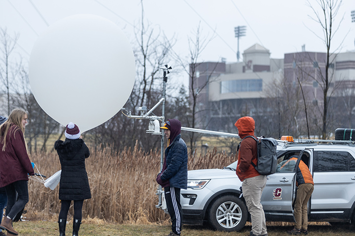 Students stand in a field near Kelly/Shorts Stadium preparing to launch a large white balloon into the air.