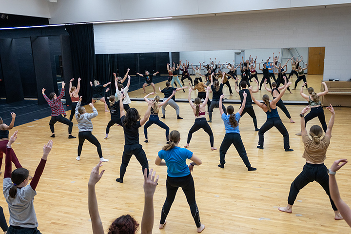 A large group of CMU dance students practice choreography inside a dance studio.