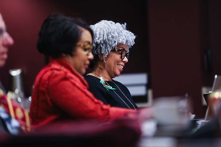 Two female Board of Trustees members sit at a large table smiling.