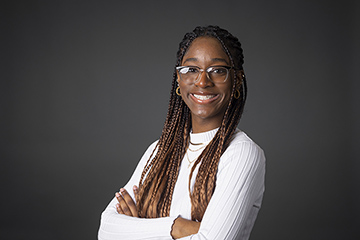 CMU student Aaliyah Howard wears a white shirt and glasses while smiling at the camera for a studio headshot.