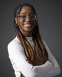 CMU student Aaliyah Howard wears a white shirt and glasses while smiling at the camera for a studio headshot.