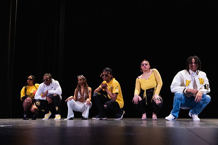 Six students crouch down on the stage while modeling student-designed fashion.