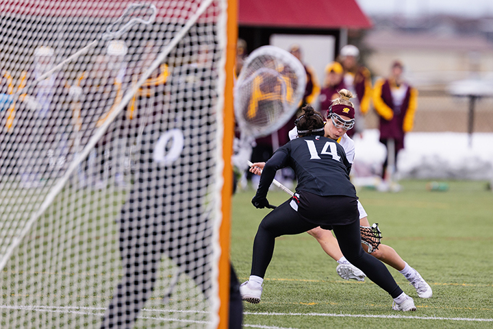 A CMU women's lacrosse player tries to run past a defender to score.