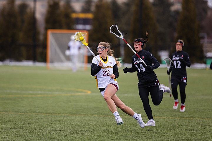 A CMU women's lacrosse player tries to run past a defender to score.