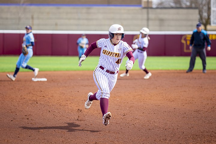 A CMU softball player in a white uniform rounds third base heading for home.