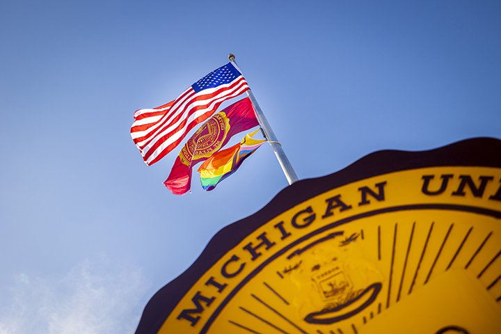 A view looking up at the CMU seal with the USA, CMU and pride flags flying from a flagpole.