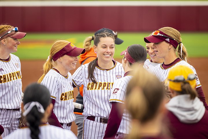 CMU softball players huddle together on the field.