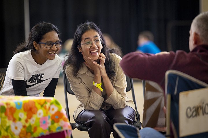 Two female students sit next to each other smiling at a caricature artist's drawing.