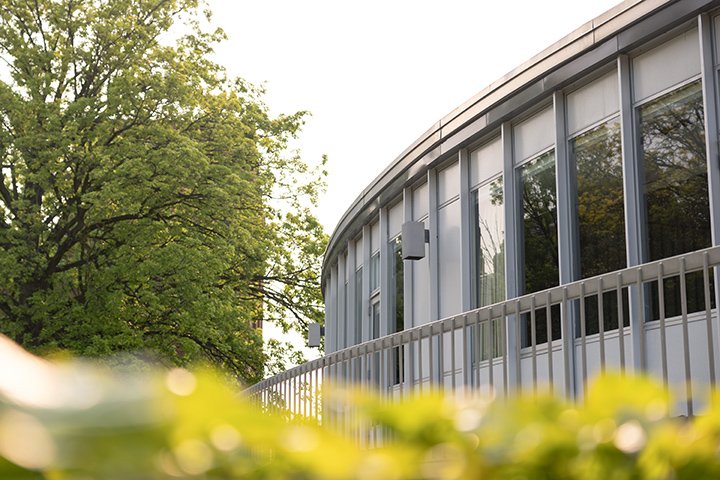 Curved windows on the back side of the University Center reflect nearby trees.