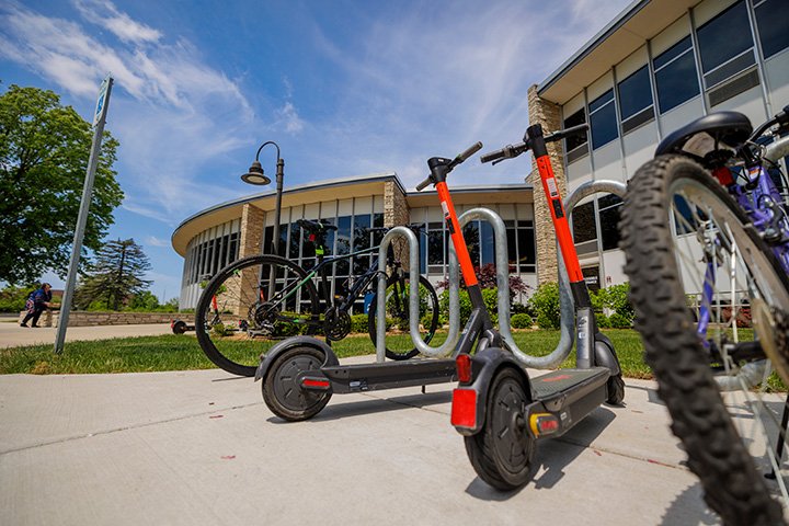 Electric scooters and bikes parked in a bike rack outside of the Bovee University Center.