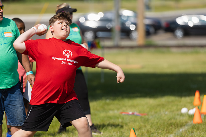 A Special Olympics Michigan athlete in a red shirt winds up to throw a softball.