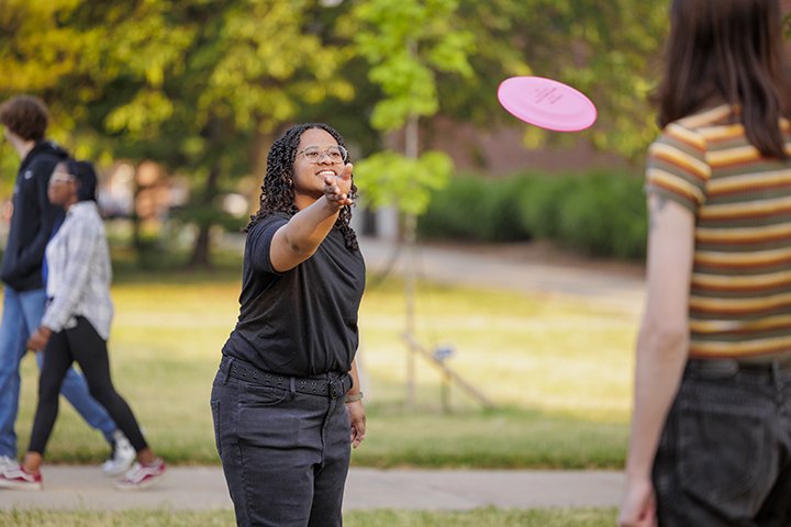 Two female students play catch with a flying disc outside.