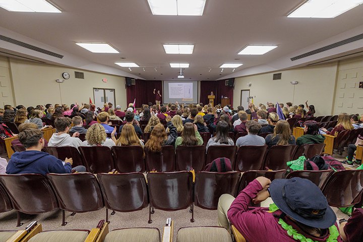 A large group of incoming freshmen sit in an auditorium watching a presentation during orientation.