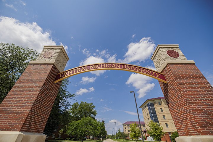 The Central Michigan University arch made of bricks with CMU logos flanking on either side, stands tall against a blue sky.