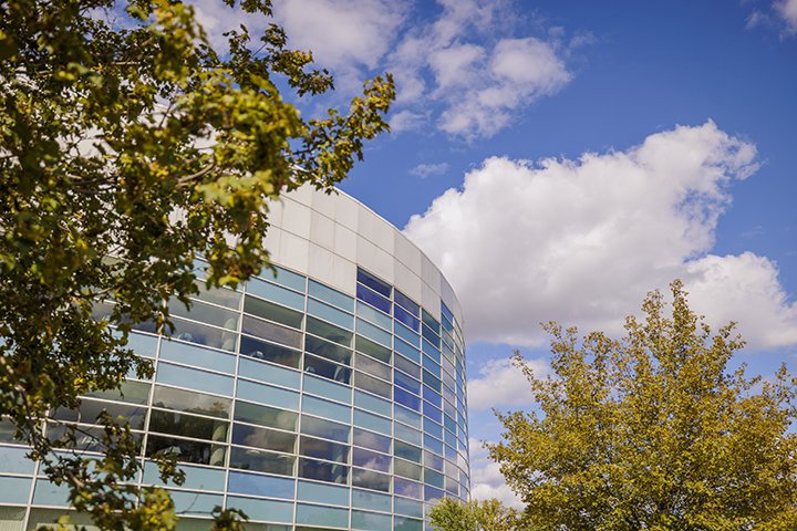 Large white clouds float high above the Charles V. Park Library as blue skies and green trees