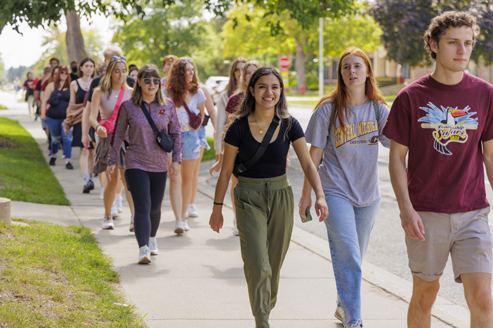 More than a dozen students walk on a sidewalk towards downtown Mt. Pleasant.