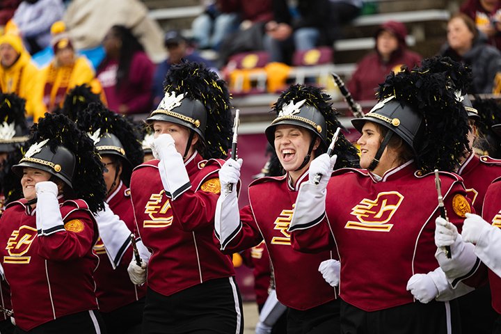 Marching band members in full uniform cheer on the field at the 2023 homecoming game.