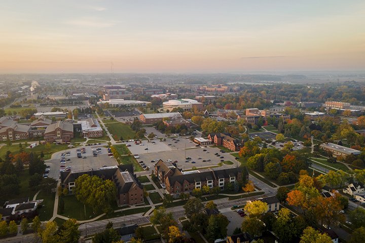 An aerial photo of Central Michigan University's campus on a foggy, fall day featuring trees changing from green to yellow, red and orange.
