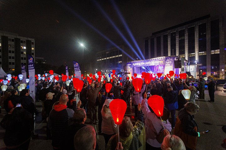 Hundreds of people gather outside at night in Grand Rapids, holding up red lights to honor those touched by blood cancers.