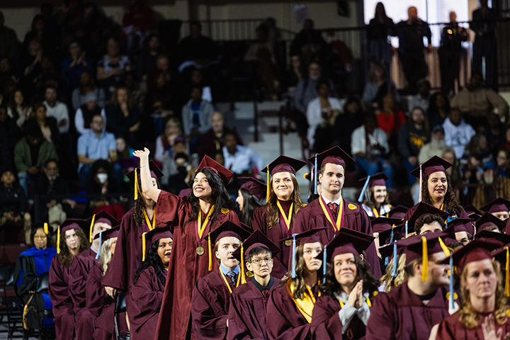 A CMU graduate stand in a crowd, waiving to family and supporters in the stands.