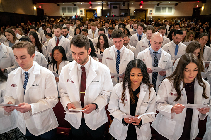 College of Medicine students stand in an auditorium talking in unison.