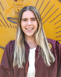 A student with long blonde hair smiles for the camera while standing in front of the CMU seal.