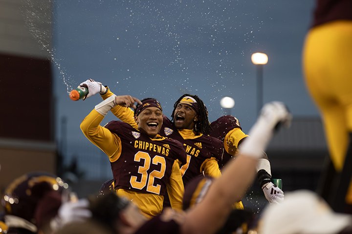 CMU football players celebrate a victory over Akron surrounded by a large group of teammates.