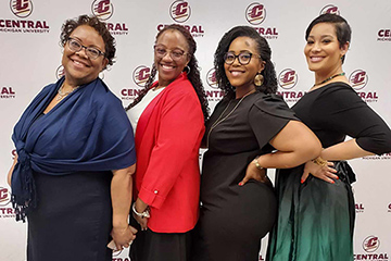 Four women stand in front of a CMU background banner smiling at the camera for a group photo..