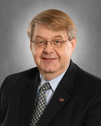 A man wearing glasses and a suit smiles at the camera.