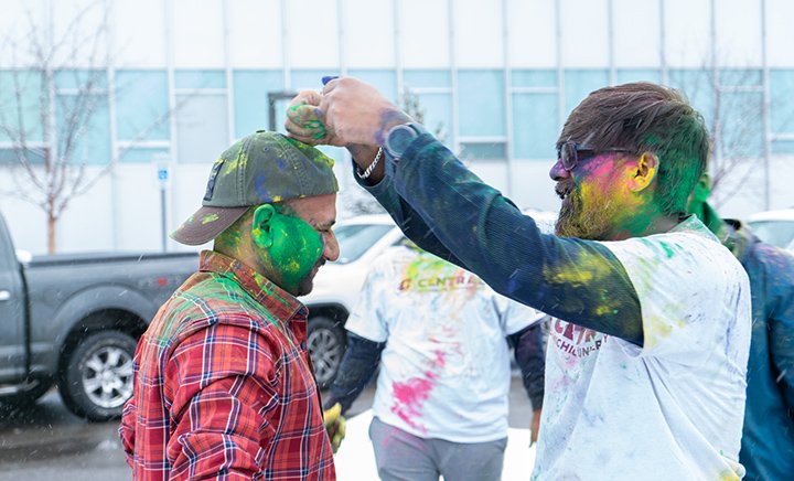 Two male students cover each other vibrant colored powders.