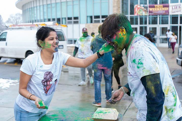 Two students cover each other vibrant colored powders.