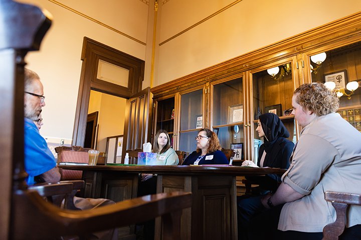 Five people sit at a rectangular table inside an office at the Michigan State Capitol Building.