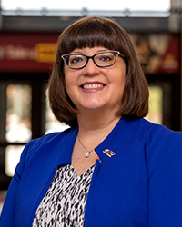 A woman in a blue jacket and glasses smiles at the camera.