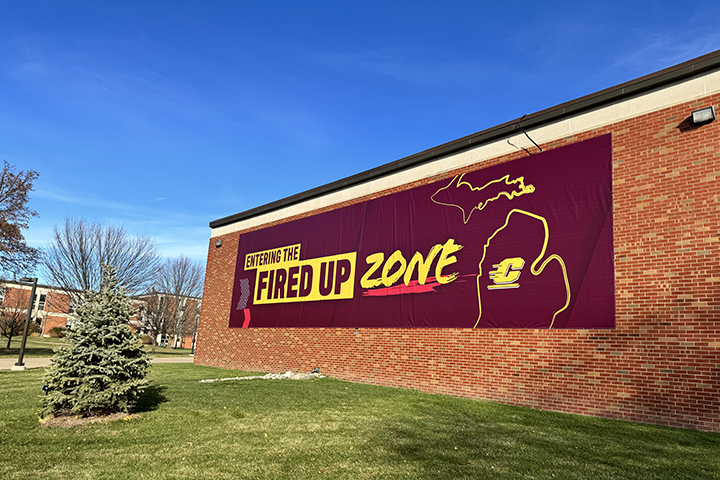 A wide angle view of a large maroon-colored vinyl sign on the side of a brick building that reads 