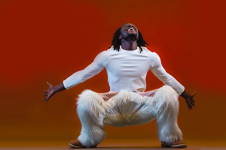 A student model wearing a white long sleeve shirt and fur-covered pants, squats while spreads his arms wide and yelling in the air.