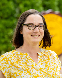 A woman wearing a yellow shirt and glasses smiles at the camera.