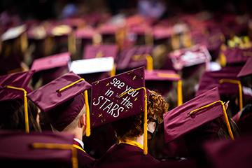 At CMU spring commencement, the backs of maroon graduation caps with tassels dangling. On one cap, the words See You In The Stars are written.
