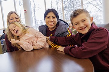 Two smiling children -- their mother in the background -- sit on either side of a smiling woman wearing CMU athletic attire.
