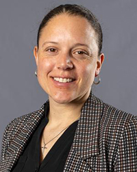 CMU's women's basketball coach Kristin Haynie wearing a checked blazer over a black blouse for a professional headshot on a gray background.