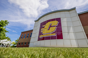 Central Michigan University's logo decorates the side of a building under a partly sunny sky and over a patch of grass.