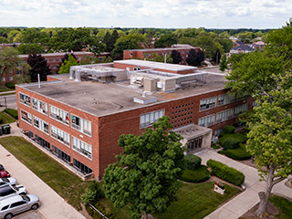 A three-story building surrounded by green trees next to a parking lot.