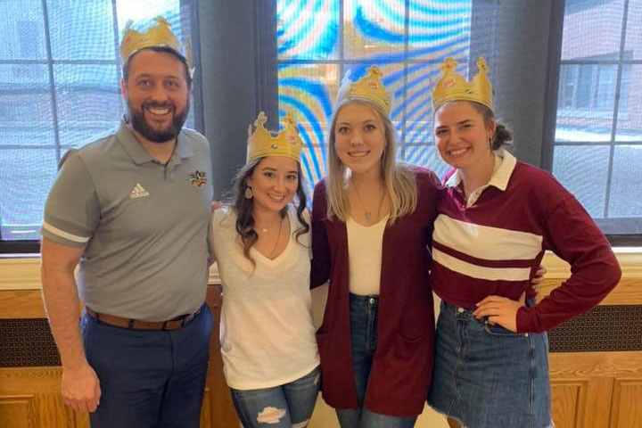 A man with facial hair and three young women smile for a group photo while wearing golden paper Burger King crowns.