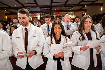 CMU medical students stand in Plachta Auditorium while taking the Hippocratic Oath during the 2023 White Coat Ceremony.