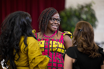 Three women have a conversation inside the University Center during the 2023 Diversity Gala. One wears a mustard-colored dress. Another wears a yellow and pink dress. The other wears a black dress.