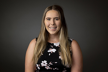 A studio headshot of Annabelle Fortine in front of a dark backdrop wearing a black dress with a floral design.