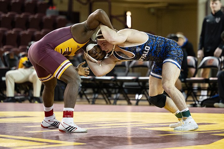 Inside McGuirk Arena, two wrestlers, one from CMU and one from Buffalo, grapple on top of a large action C logo.