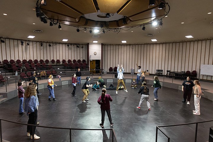 Approximately a dozen students stand in a large circle inside a large, round room taking part in an improv workshop with actor and CMU alum Larry Joe Campbell.